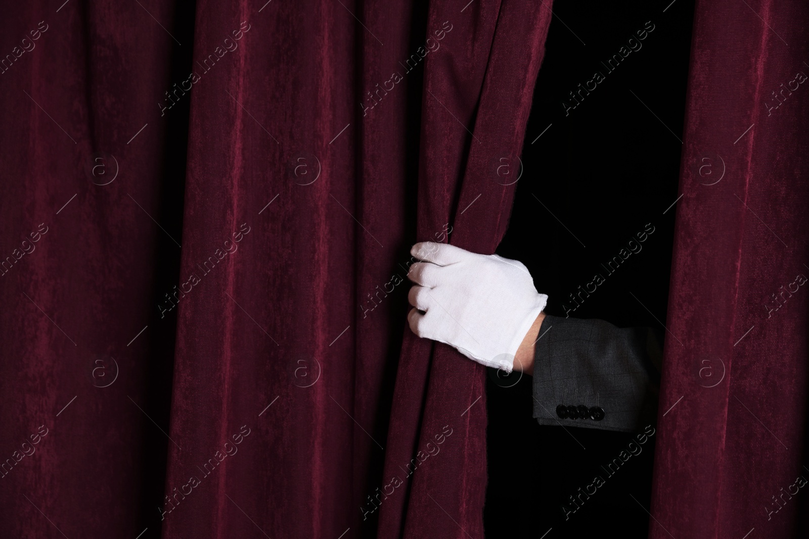 Photo of Man closing red front curtains in theatre, closeup