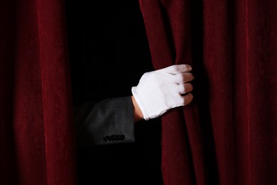 Photo of Man closing red front curtains in theatre, closeup