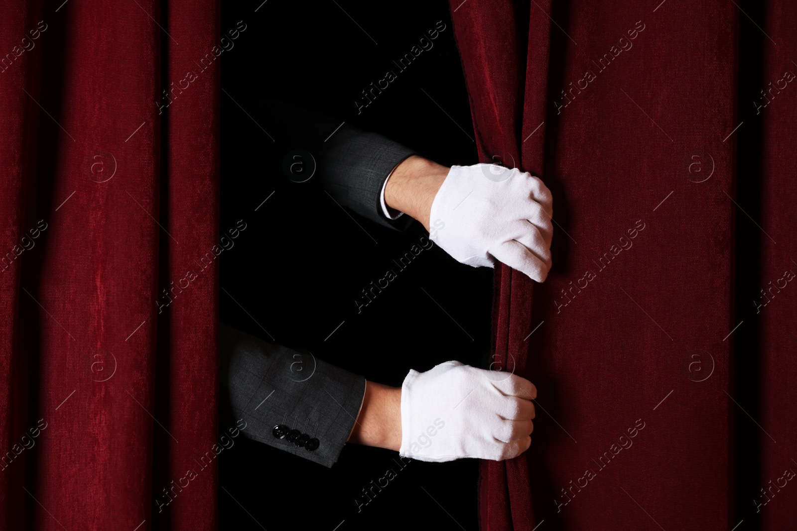 Photo of Man closing red front curtains in theatre, closeup