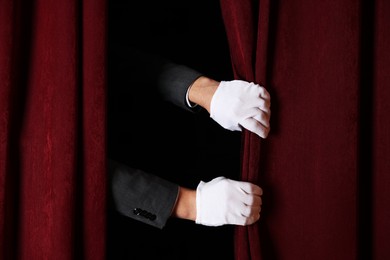 Photo of Man closing red front curtains in theatre, closeup