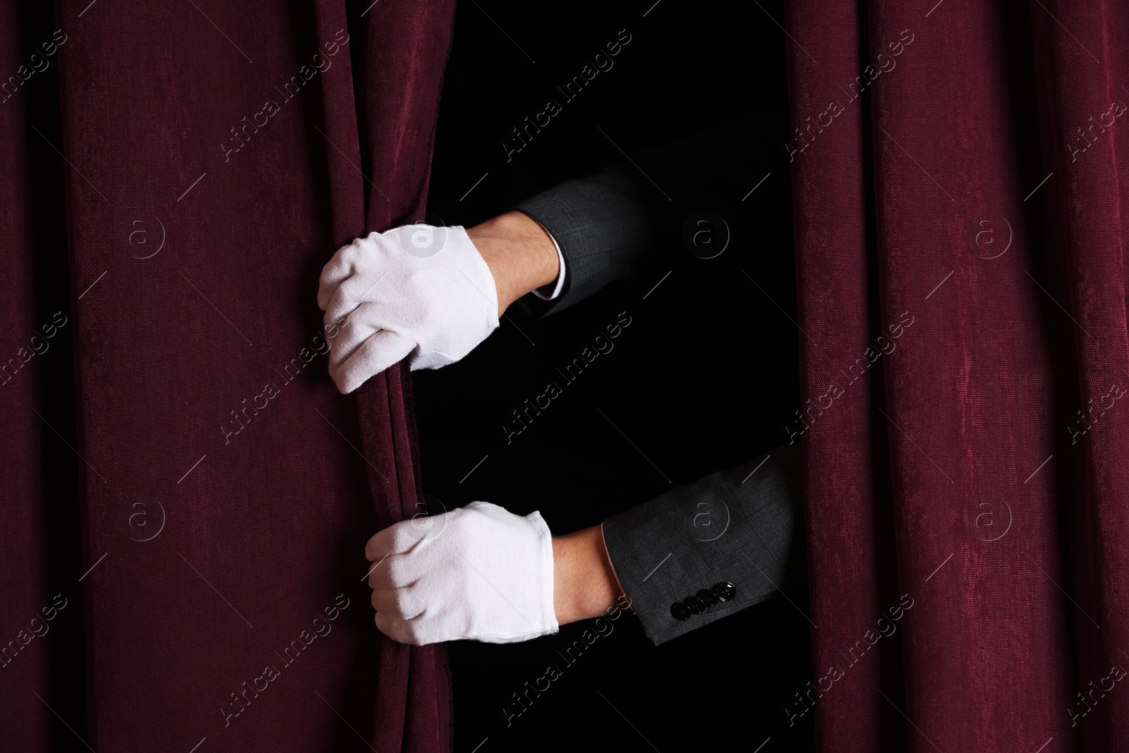 Photo of Man closing red front curtains in theatre, closeup