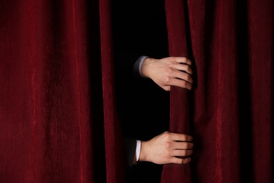 Photo of Man closing red front curtains in theatre, closeup