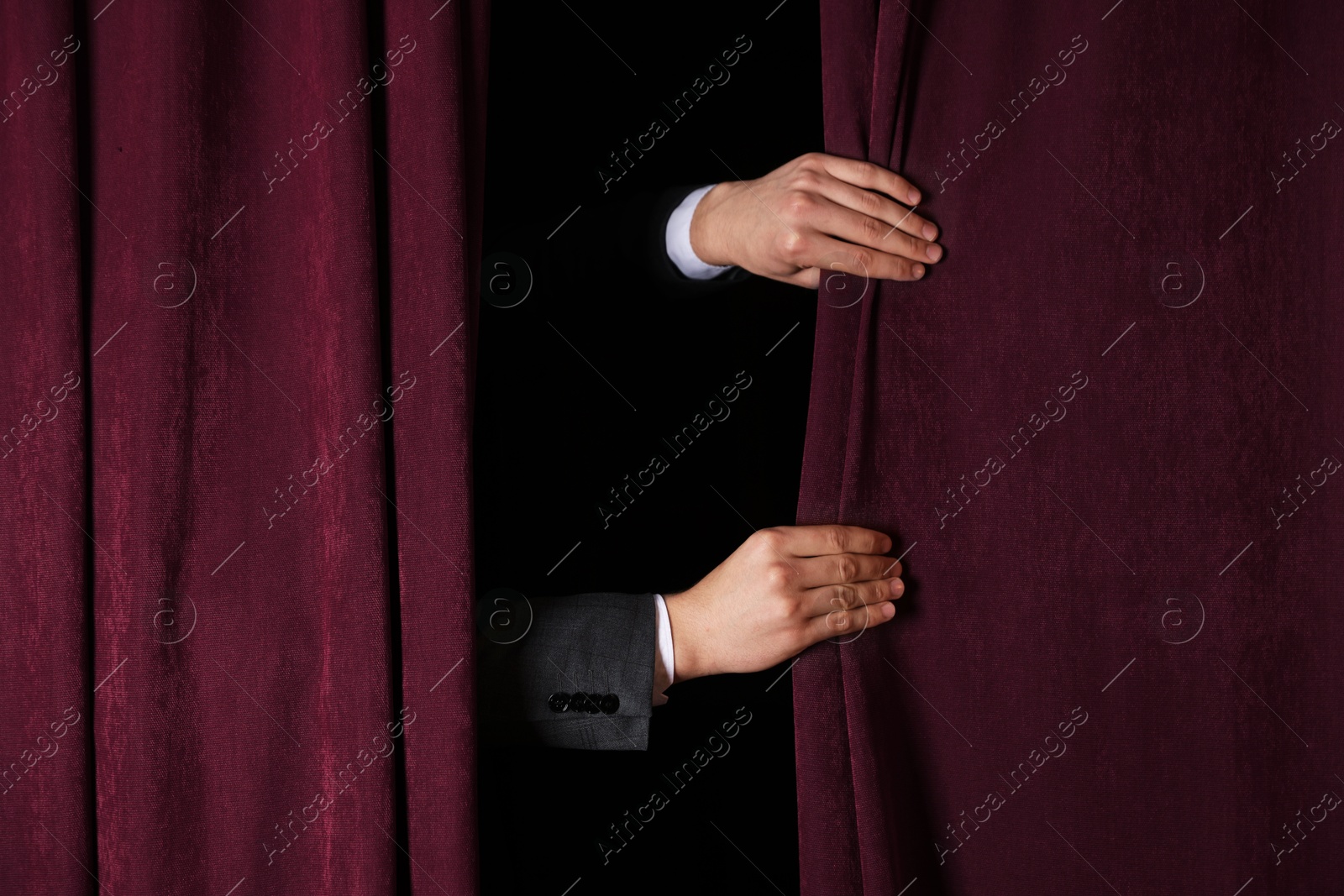 Photo of Man closing red front curtains in theatre, closeup