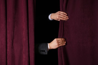 Photo of Man closing red front curtains in theatre, closeup