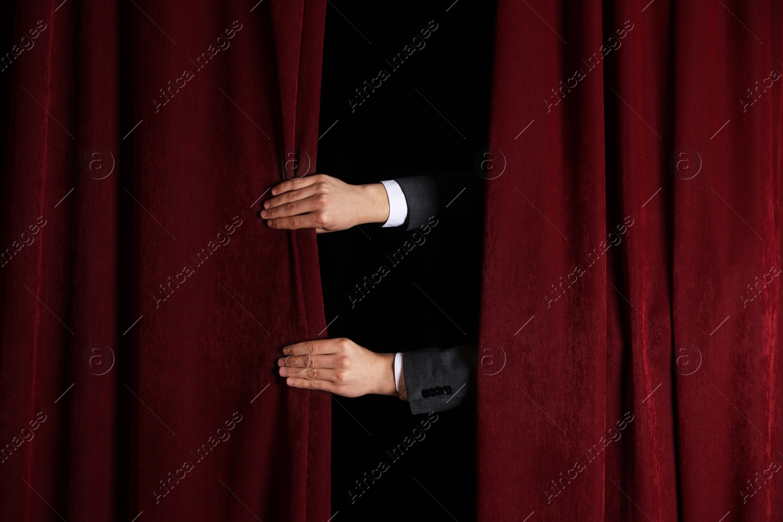 Photo of Man closing red front curtains in theatre, closeup