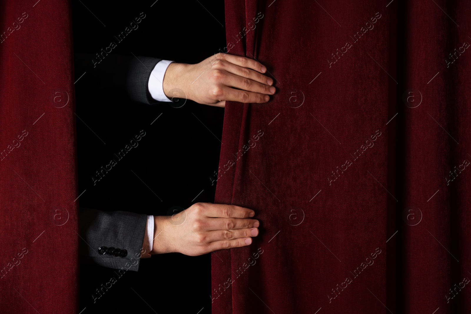 Photo of Man closing red front curtains in theatre, closeup