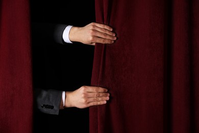 Photo of Man closing red front curtains in theatre, closeup