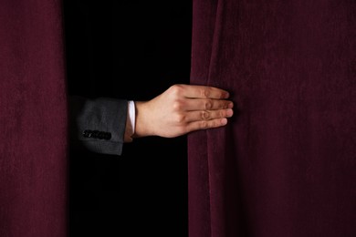 Photo of Man closing red front curtains in theatre, closeup