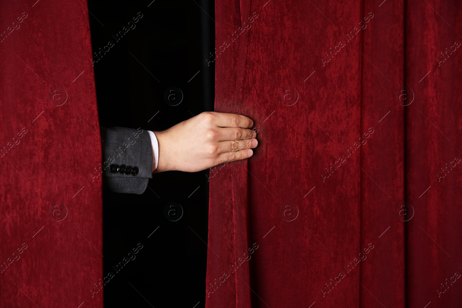 Photo of Man closing red front curtains in theatre, closeup