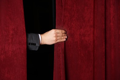 Photo of Man closing red front curtains in theatre, closeup