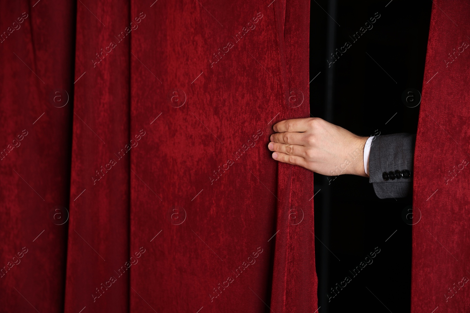 Photo of Man closing red front curtains in theatre, closeup