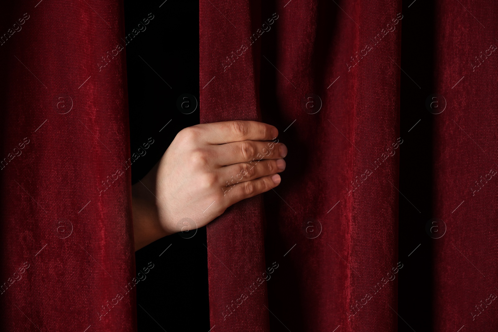 Photo of Man closing red front curtains in theatre, closeup