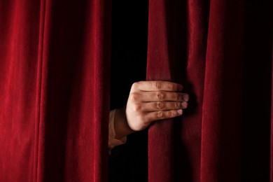 Photo of Man closing red front curtains in theatre, closeup