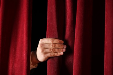 Photo of Man closing red front curtains in theatre, closeup