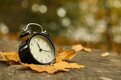 Photo of Autumn time. Alarm clock on tree stump in park, closeup with space for text