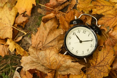 Photo of Autumn time. Alarm clock on fallen leaves, top view with space for text