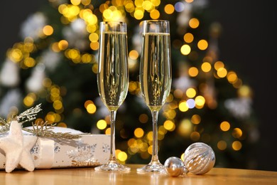 Photo of Champagne in glasses and decor on wooden table against blurred Christmas lights, bokeh effect