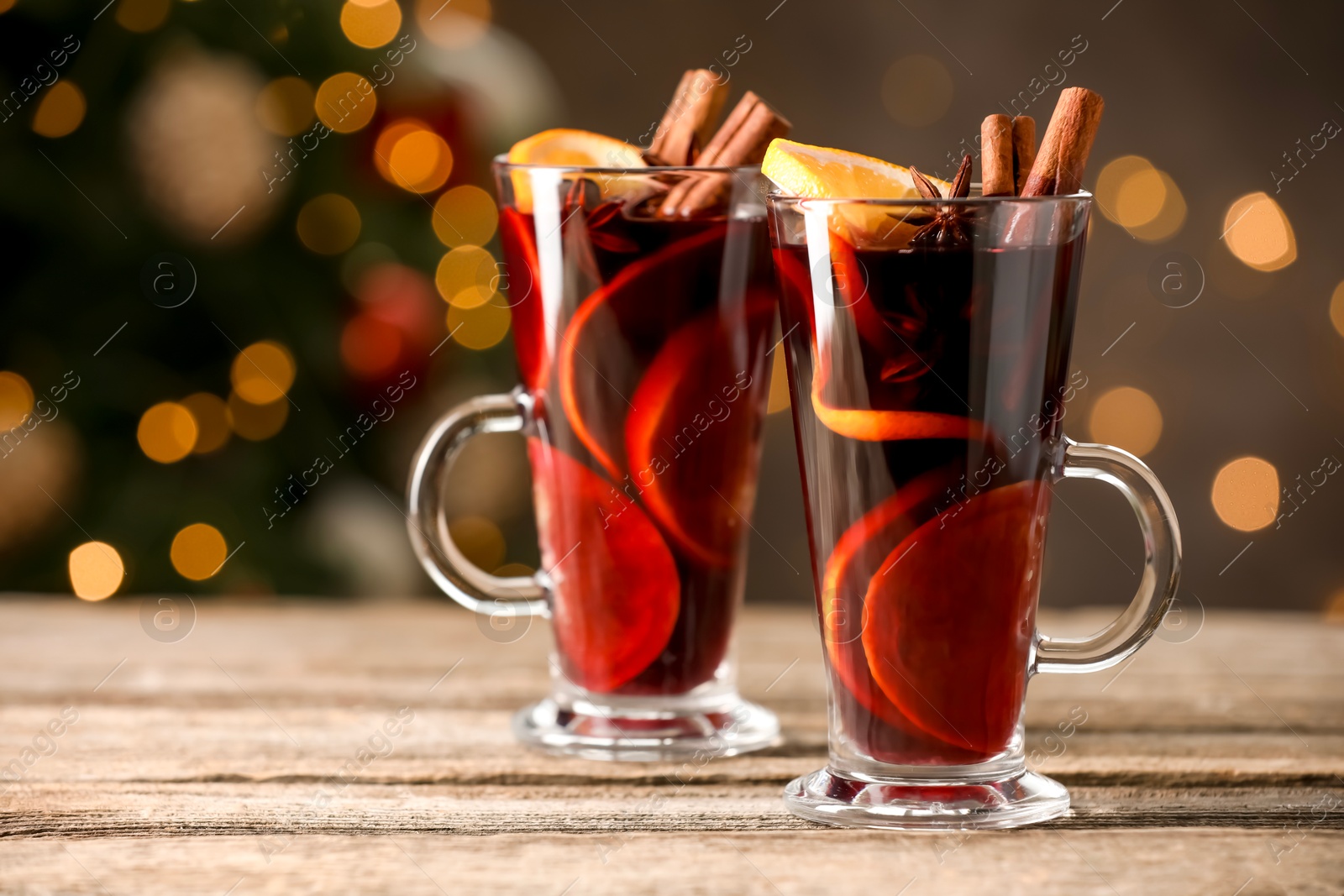 Photo of Tasty mulled wine with spices on wooden table against blurred Christmas lights, space for text. Bokeh effect