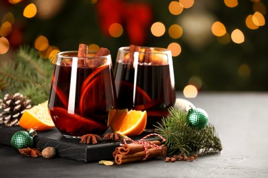 Photo of Tasty mulled wine with spices and Christmas decor on grey table, bokeh effect