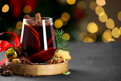 Photo of Tasty mulled wine with spices, cookies and decor on grey table against blurred Christmas lights, space for text. Bokeh effect