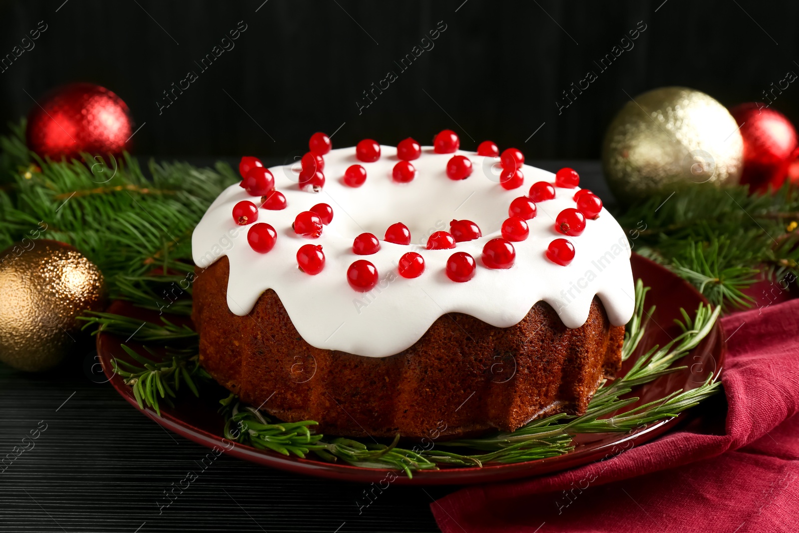 Photo of Tasty Christmas cake with red currants and rosemary on black wooden table, closeup