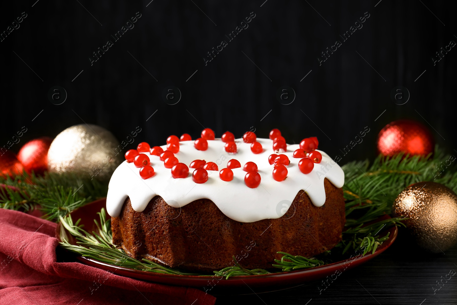 Photo of Tasty Christmas cake with red currants and rosemary on black wooden table, closeup