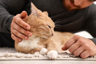 Photo of Man petting cute ginger cat on floor at home, closeup