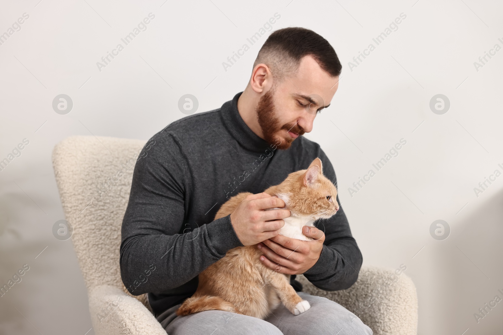 Photo of Man petting cute ginger cat on armchair at home