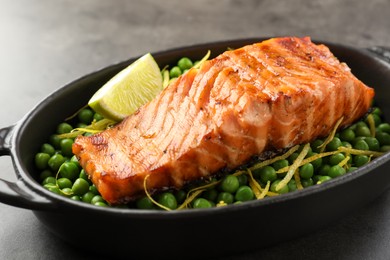 Photo of Delicious grilled salmon fillet with green peas and lime in baking dish on grey table, closeup