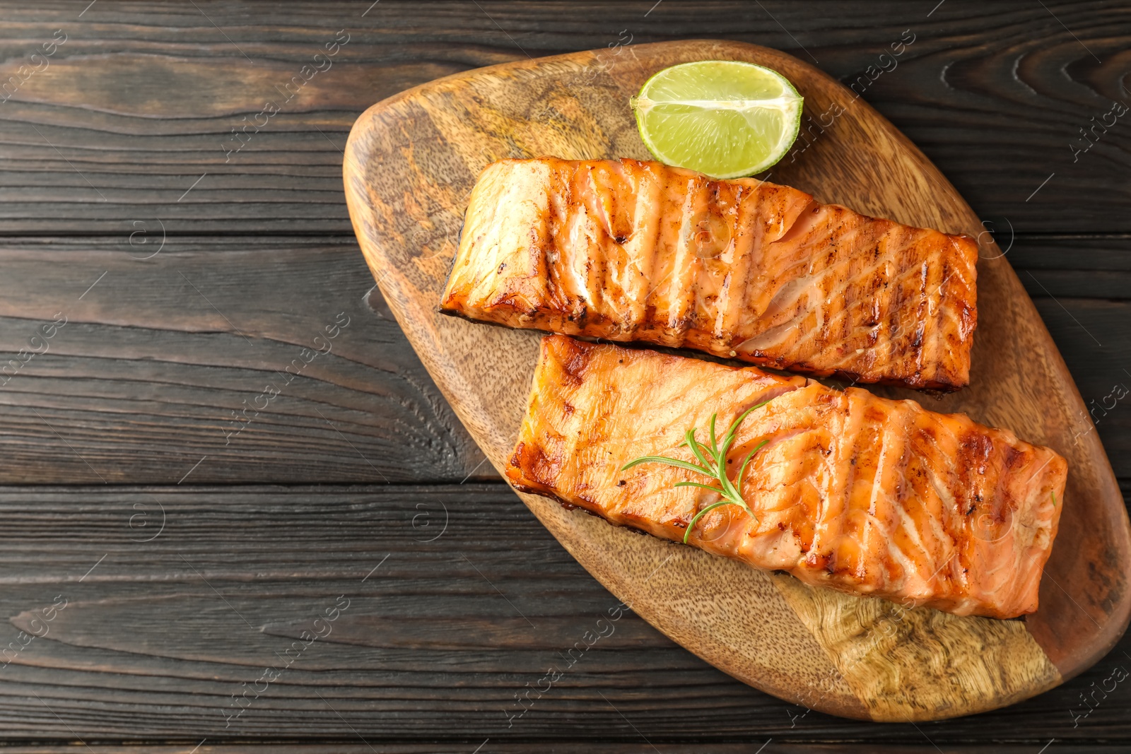 Photo of Delicious grilled salmon fillets with lime and rosemary on wooden table, top view. Space for text