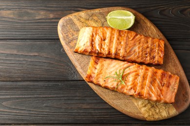 Photo of Delicious grilled salmon fillets with lime and rosemary on wooden table, top view. Space for text