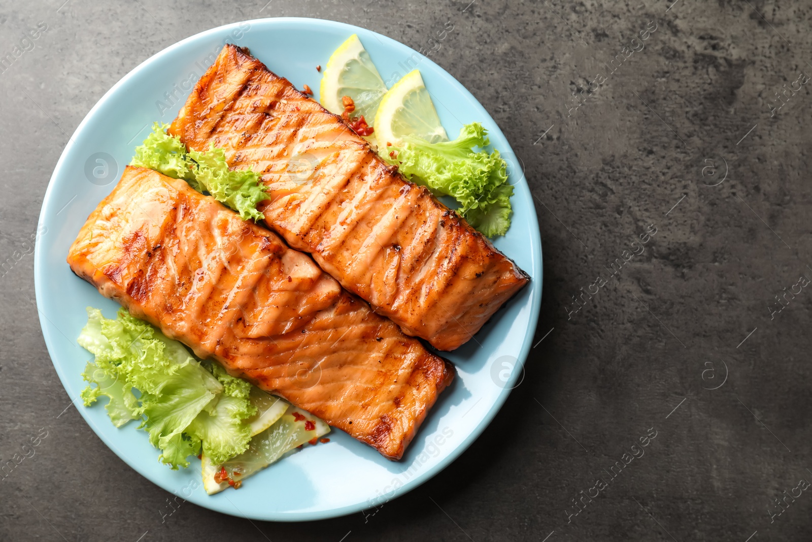 Photo of Delicious grilled salmon fillets with lettuce and lemon on grey table, top view. Space for text