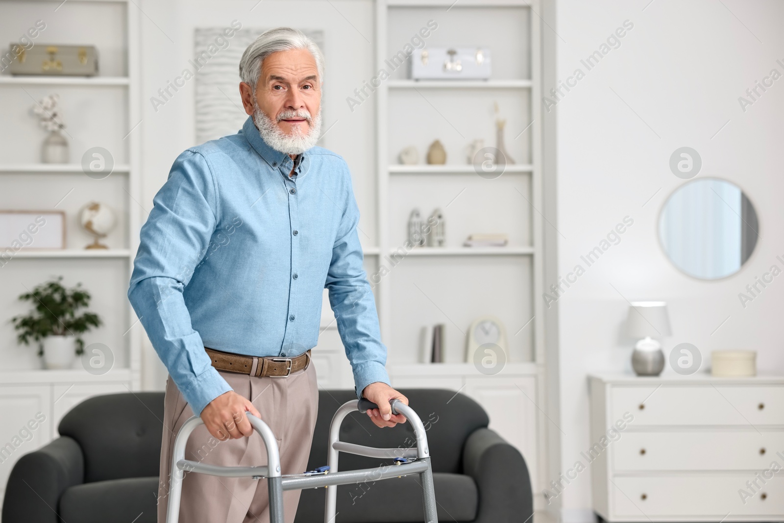 Photo of Senior man using walking frame at home. Space for text