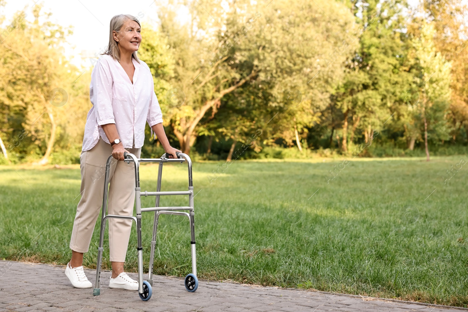 Photo of Senior woman with walking frame in park, space for text