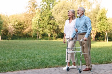 Photo of Senior couple with walking frame in park, space for text