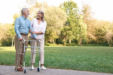 Senior couple with walking frame in park, space for text