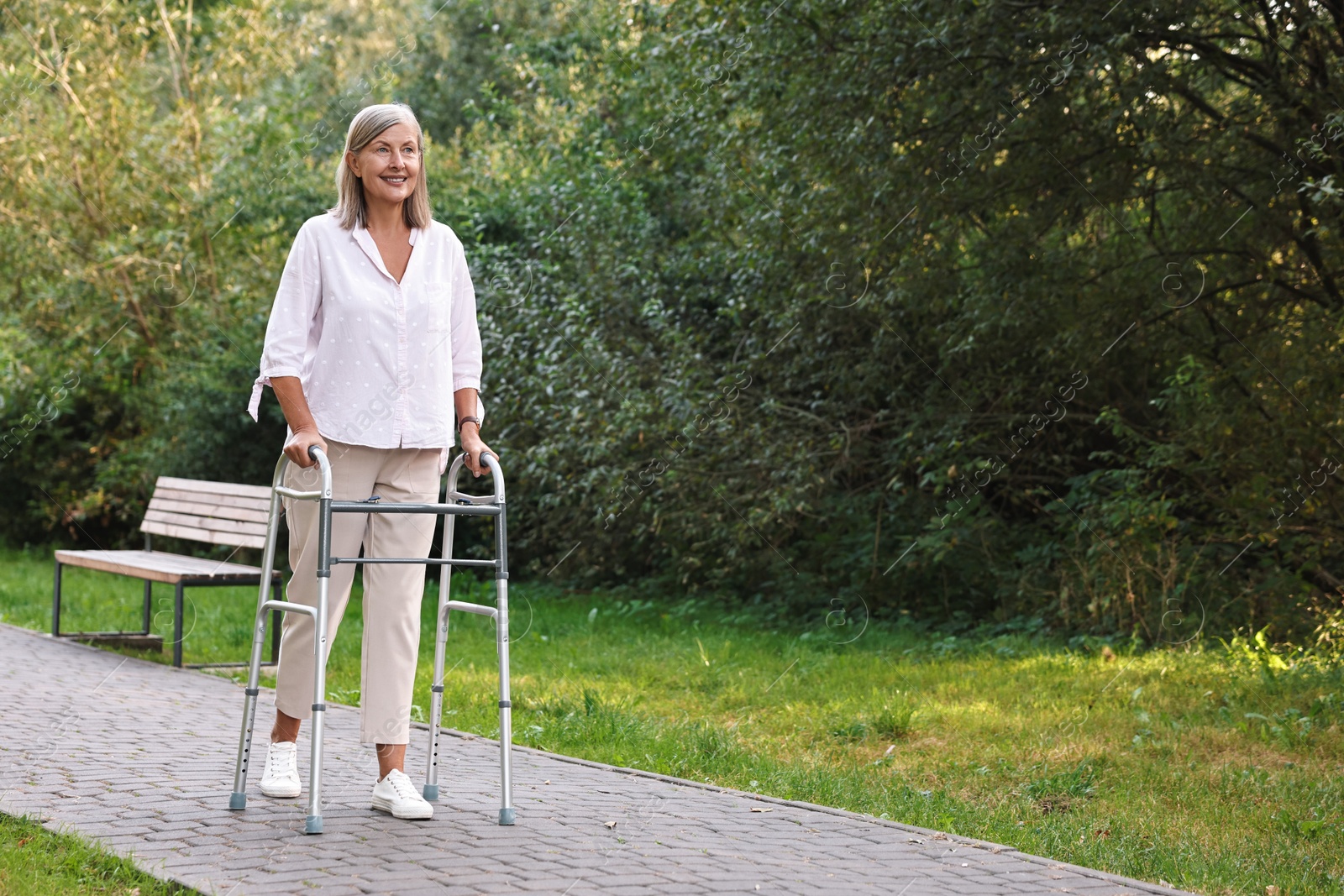 Photo of Senior woman with walking frame in park, space for text