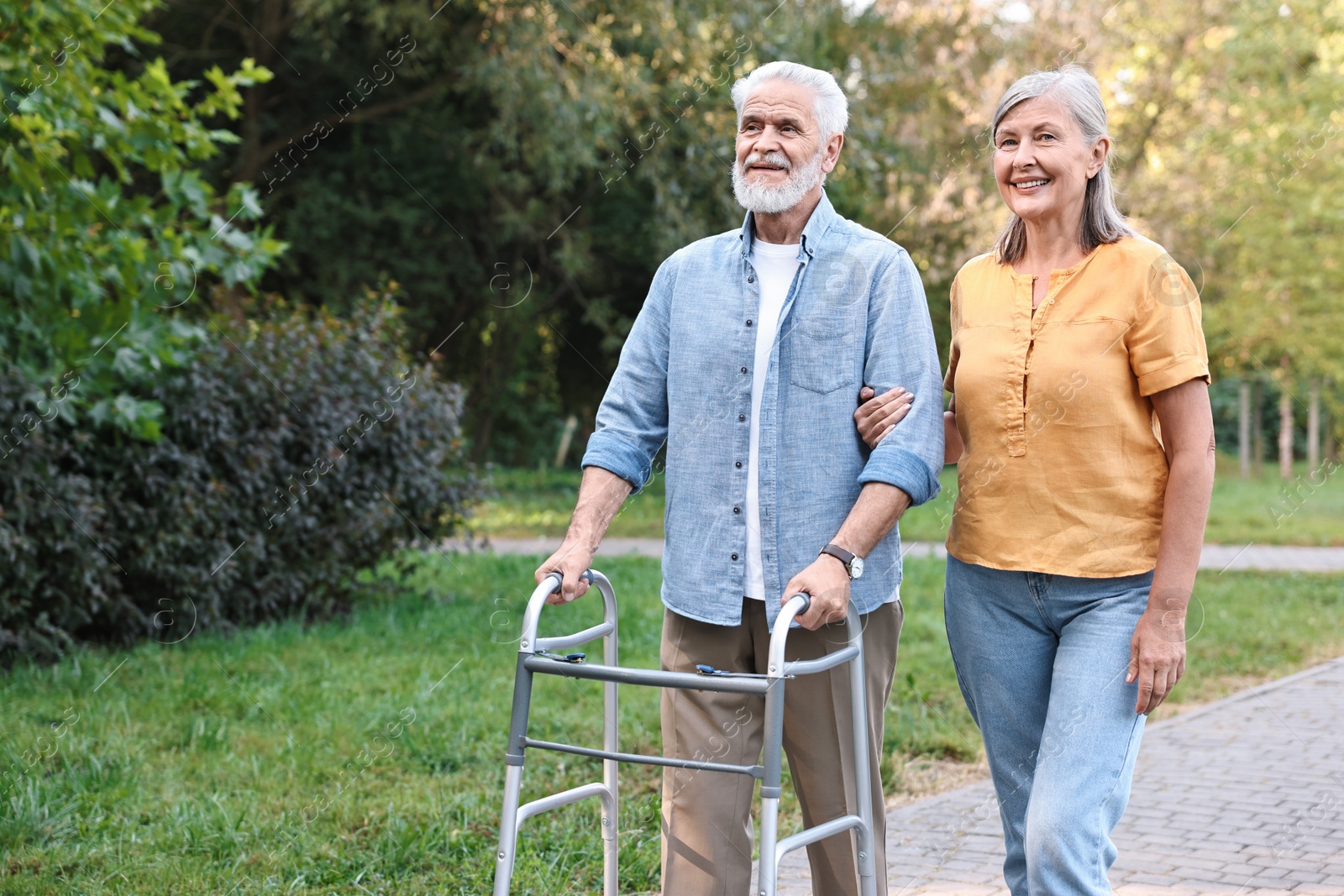 Photo of Senior couple with walking frame in park, space for text