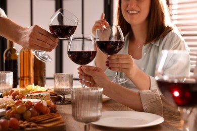 Photo of People clinking glasses of red wine at served table, closeup