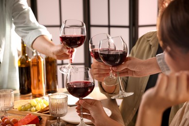 Photo of People clinking glasses of red wine at served table, closeup