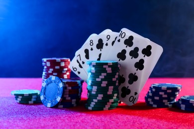 Photo of Poker chips and playing cards on pink table