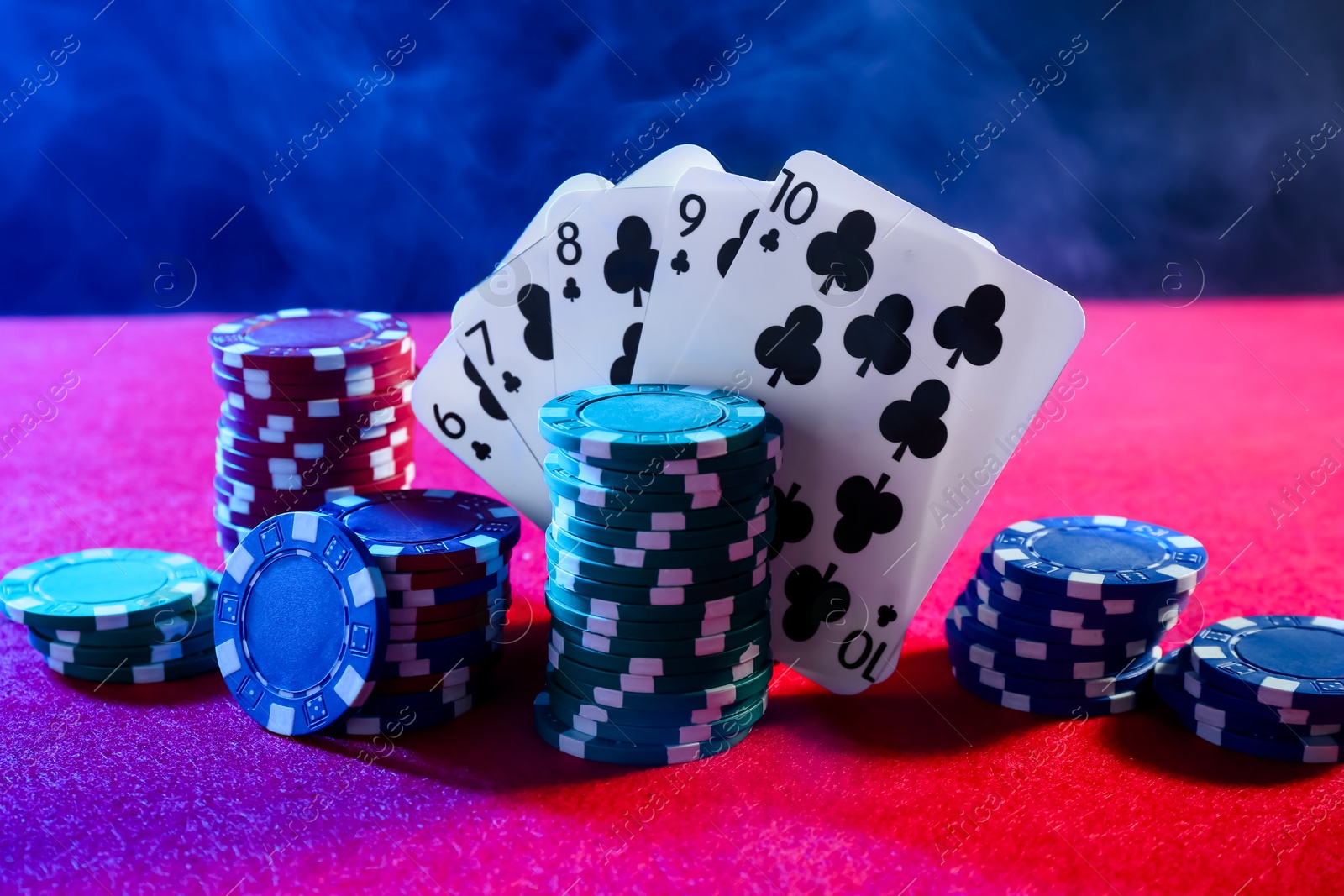 Photo of Poker chips and playing cards on pink table