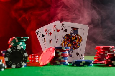 Photo of Poker chips, dice and playing cards on green table in neon lights, closeup