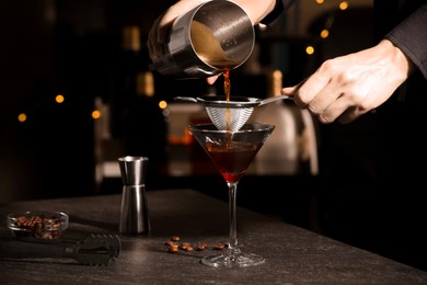 Photo of Bartender making delicious espresso martini at dark table against blurred lights, closeup