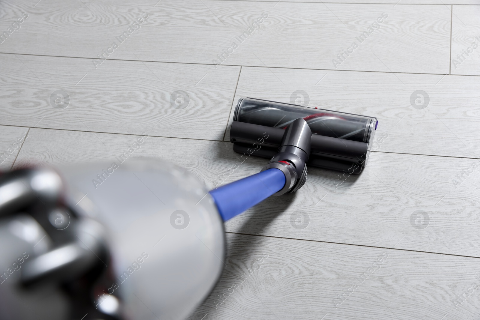 Photo of Cleaning floor with cordless vacuum cleaner indoors, closeup