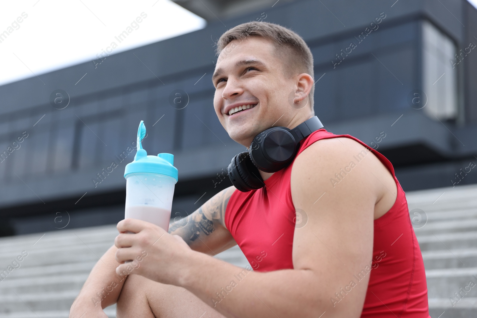 Photo of Smiling man with shaker of protein drink outdoors, low angle view