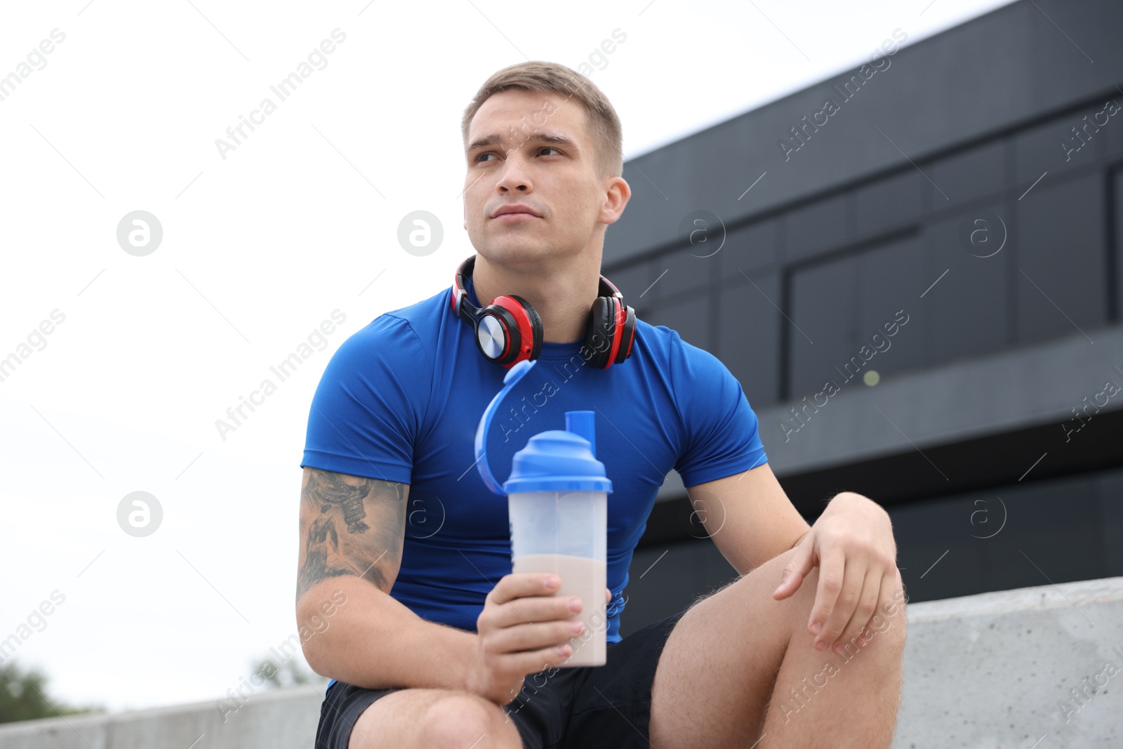 Photo of Athletic man with shaker of protein drink outdoors, low angle view