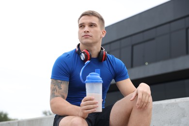 Photo of Athletic man with shaker of protein drink outdoors, low angle view