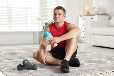 Photo of Athletic man with shaker of protein drink sitting on carpet at home