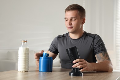 Photo of Making protein cocktail. Man with scoop of powder and shaker at wooden table